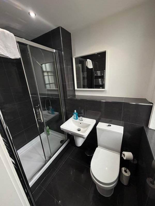Modern bathroom with black tile walls, shower enclosure, white sink and toilet