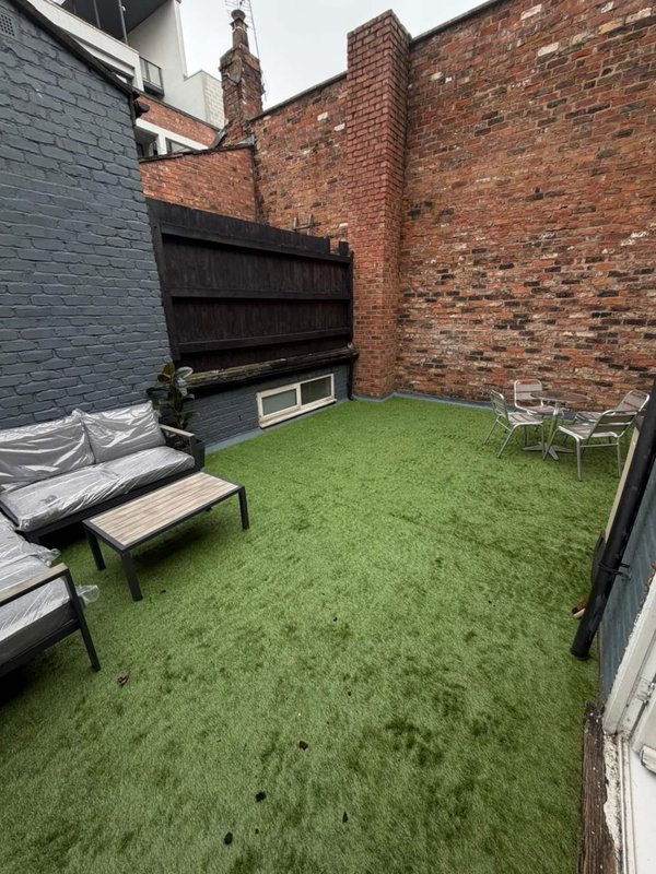 Paved courtyard with artificial grass, wooden seating, brick walls and chimney