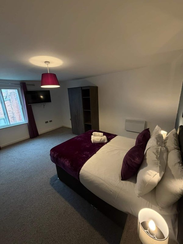 Hotel bedroom with double bed, burgundy pendant light, armchair and window