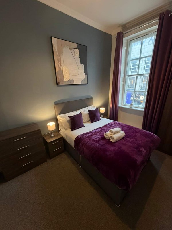 Modern bedroom with double bed, purple throw, bedside lamps and framed wall art
