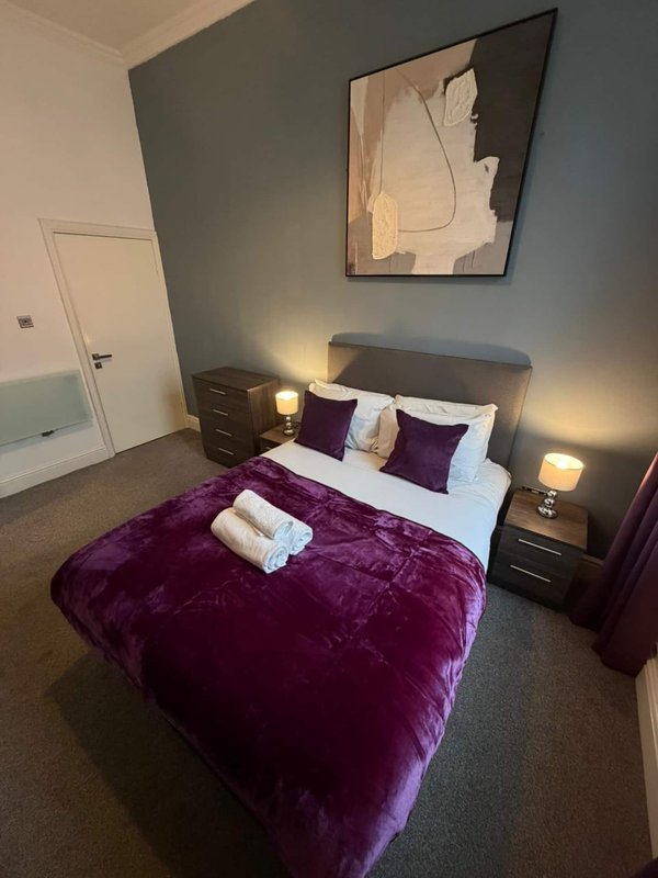 Modern bedroom with purple velvet bed, grey headboard, bedside lamps and framed wall art
