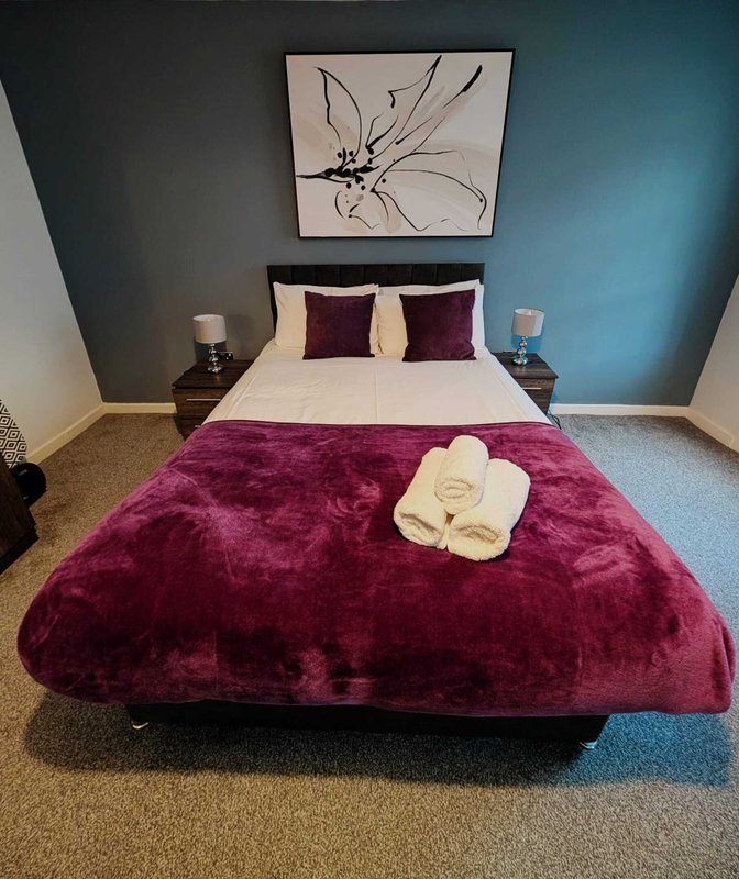 Modern bedroom with double bed, burgundy bedding, white pillows, and framed artwork above