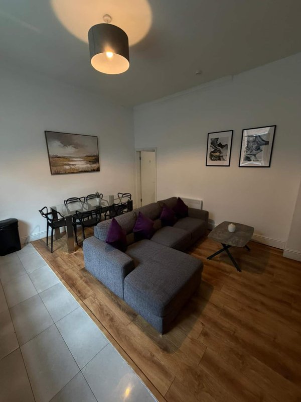 Open-plan living room with grey sofa, dining table, framed wall art, wooden flooring and ceiling light