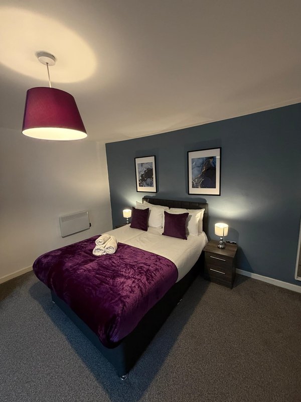 Modern bedroom with double bed, purple velvet throw, burgundy pendant lamp and framed wall art