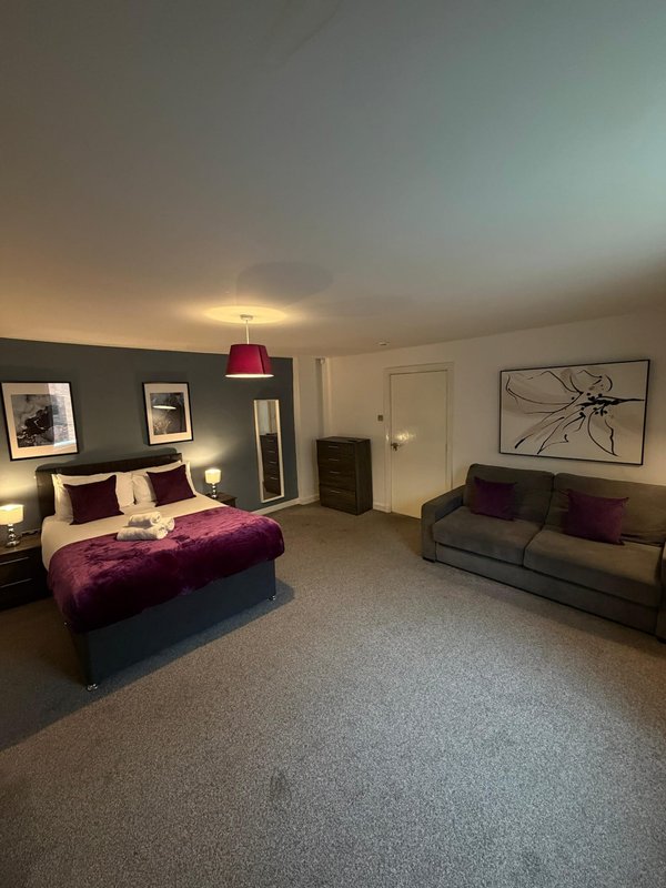 Spacious bedroom with double bed, burgundy bedding, gray sofa, and wall art