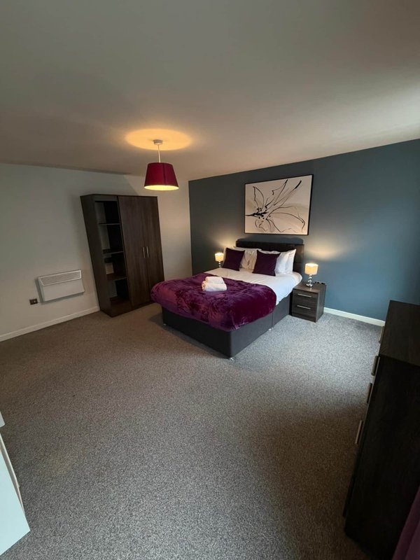 Bedroom with double bed, purple bedding, pendant light, teal accent wall and wooden furniture