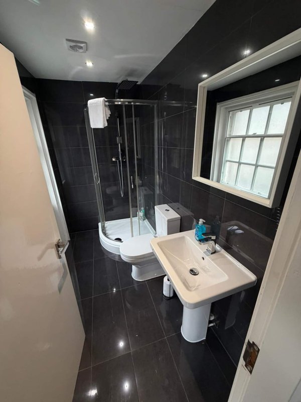 Modern bathroom with black tile walls, white sink, toilet, shower enclosure and window