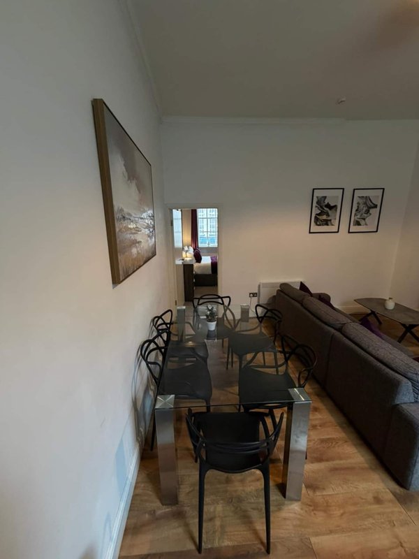 Open-plan living and dining area with glass table, black chairs, brown sofa and framed wall art