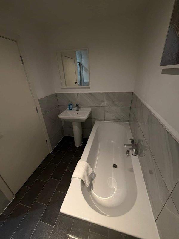 Bathroom with bathtub, pedestal sink, mirror and dark tile flooring
