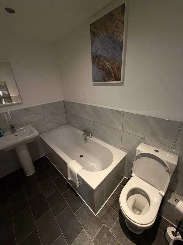 Bathroom with white bathtub, toilet, pedestal sink and grey tile walls