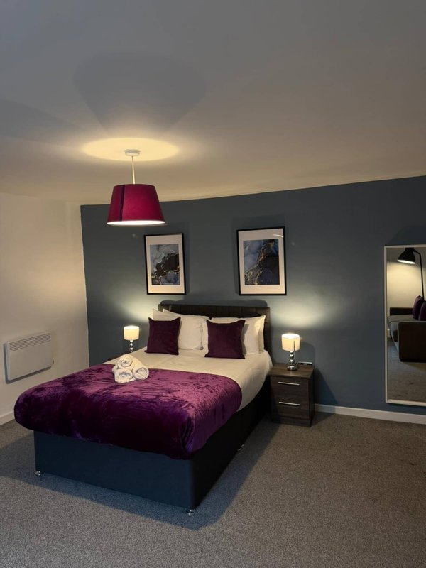 Modern bedroom with double bed, purple velvet throw, dark feature wall and pendant light