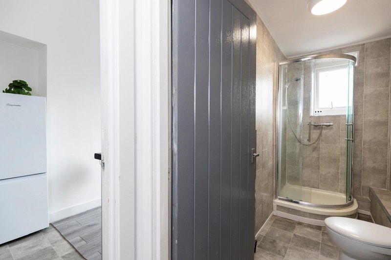 Modern bathroom with curved glass shower enclosure, toilet, and beige tile walls