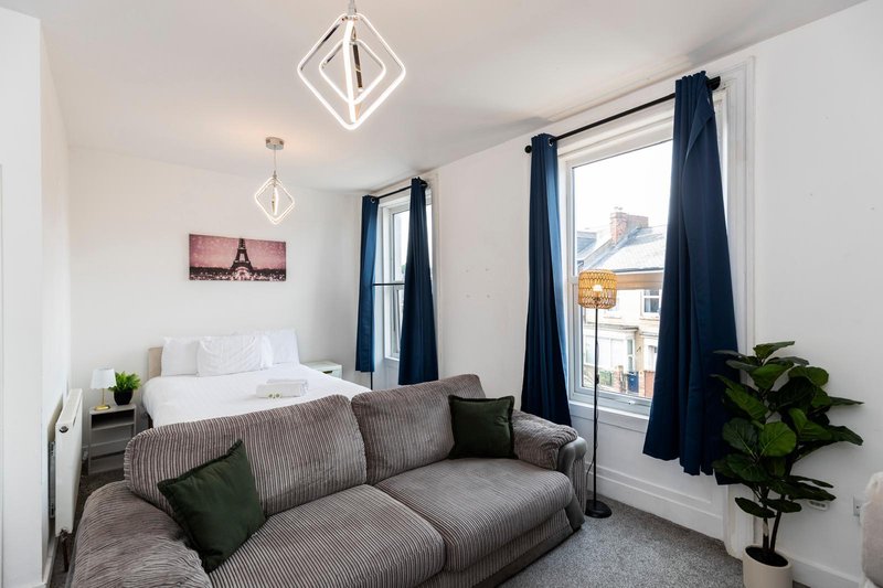 Modern studio bedroom with gray sofa, white bed, dark blue curtains and pendant lighting