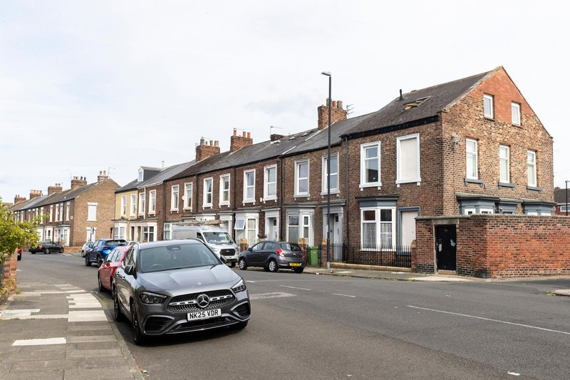 Street view of traditional brick terraced houses with parked cars and clear sky