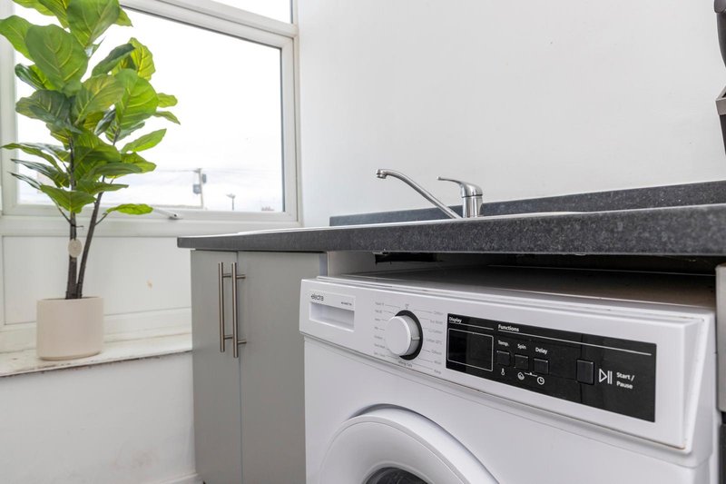 Modern laundry room with white washing machine, dark countertop, potted plant and window