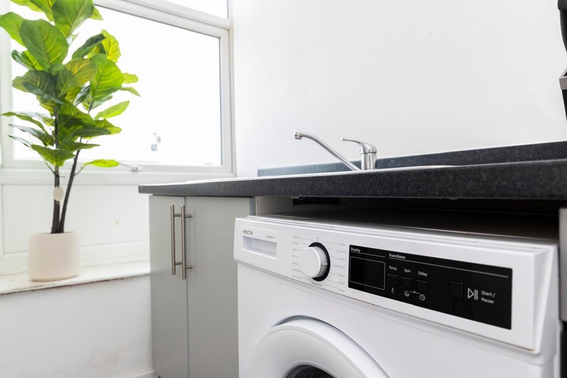 Modern laundry room with white washing machine, black countertop, and potted plant by window