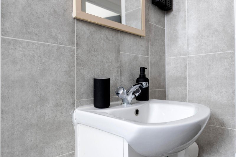 Modern bathroom with white sink, black tap, mirror and grey tile walls