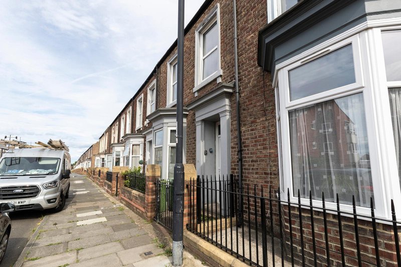 Brick terraced house with black railings, white door frame and bay window on residential street