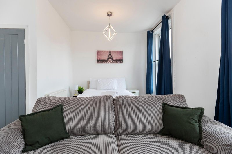Bedroom with grey upholstered bed, green cushions, pendant light, and dark blue curtains
