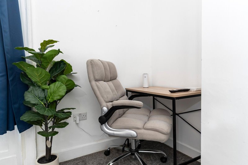 Home office workspace with grey office chair, desk, potted plant and blue curtain
