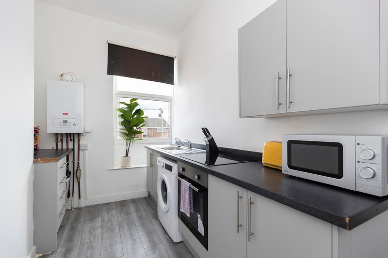 Modern kitchen with white cabinetry, black countertop, integrated appliances and window