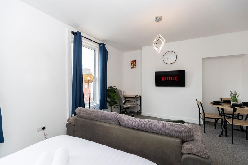 Open-plan living area with sofa, dining table, wall-mounted TV and window with blue curtains