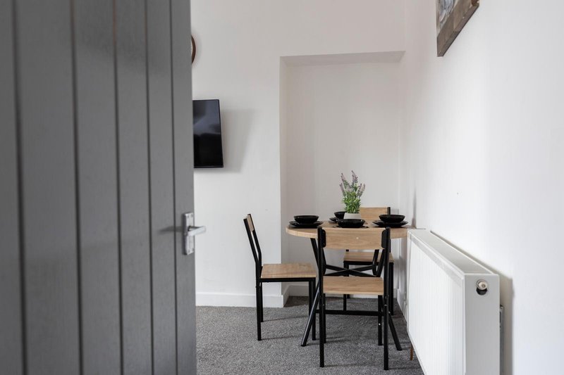 Modern dining nook with wooden table, black chairs, potted plant, and gray door