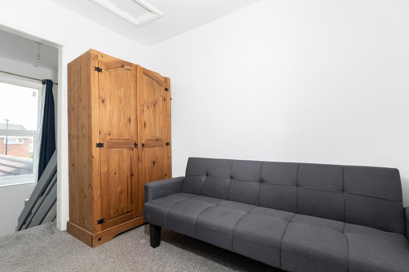 Bright bedroom with dark grey sofa, wooden wardrobe, and window with city view