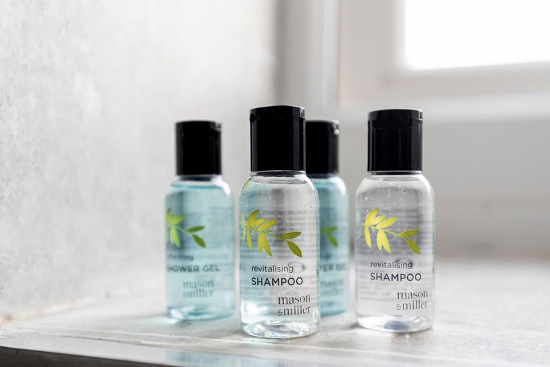 Bathroom shelf with four clear bottles of toiletries and shampoo products