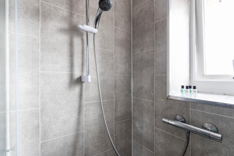 Modern bathroom shower with grey tile walls, rainfall showerhead and window with toiletries shelf