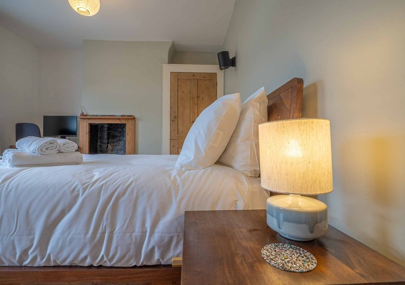 Bedroom with white bedding, wooden headboard, bedside lamp, and fireplace