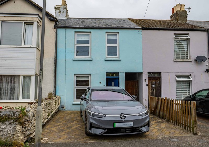 Colorful terraced house with driveway, parked car, and wooden fence