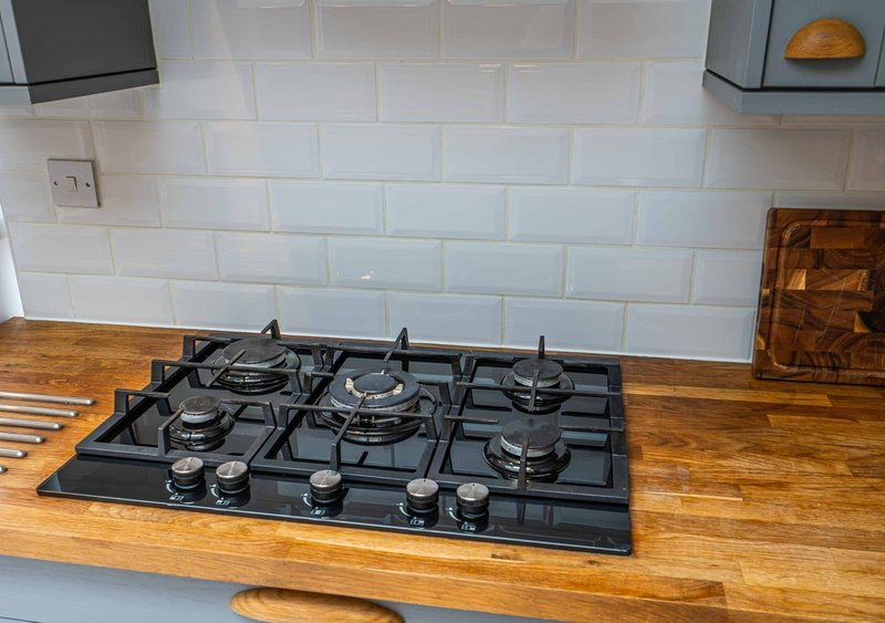Modern kitchen with black gas hob on wooden countertop, white subway tile backsplash