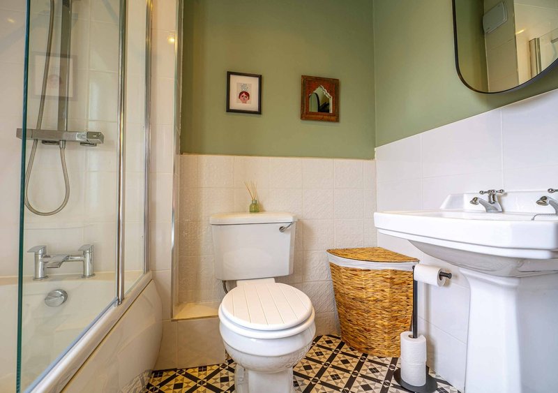 Bathroom with toilet, pedestal sink, shower enclosure, wicker basket and framed wall art