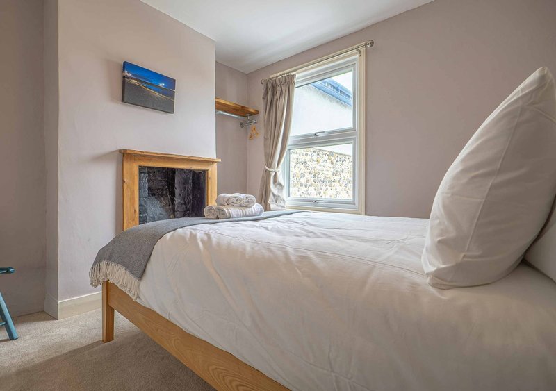 Bright bedroom with wooden bed, white bedding, fireplace, and large window with garden view