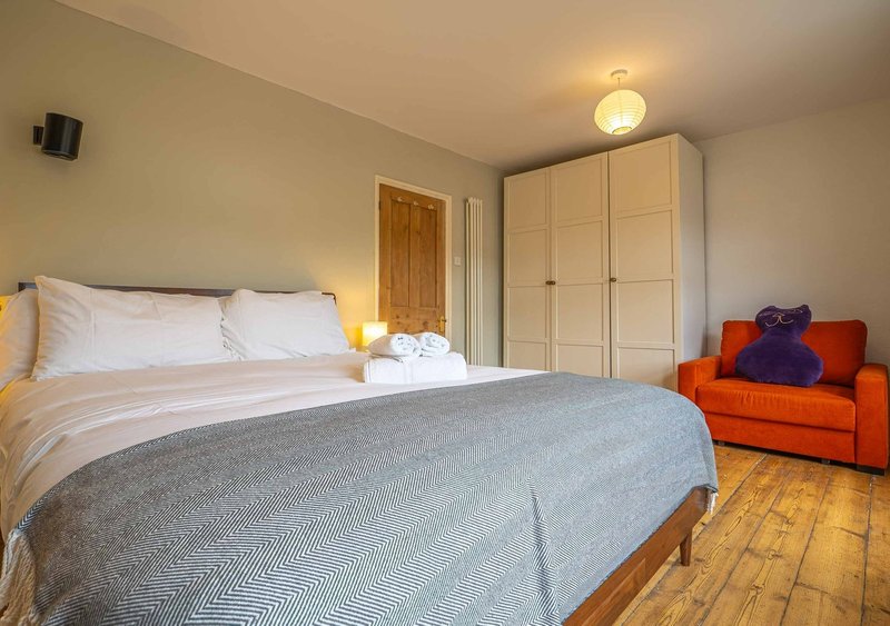 Bright bedroom with double bed, wooden wardrobe, orange armchair and wooden floor