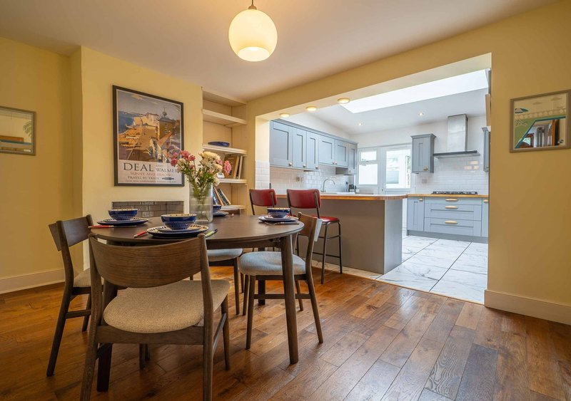 Dining room with wooden table, chairs, and open-plan view into modern kitchen with yellow walls