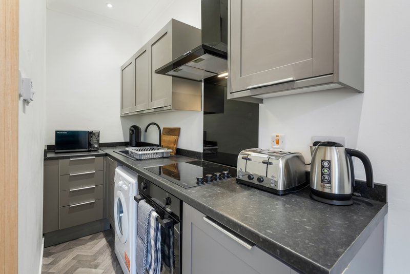 Modern kitchen with gray cabinets, black countertop, appliances and kettle