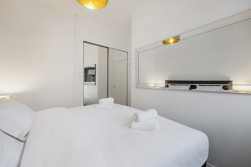 Compact modern bedroom with white double bed, mirror, and ensuite bathroom door