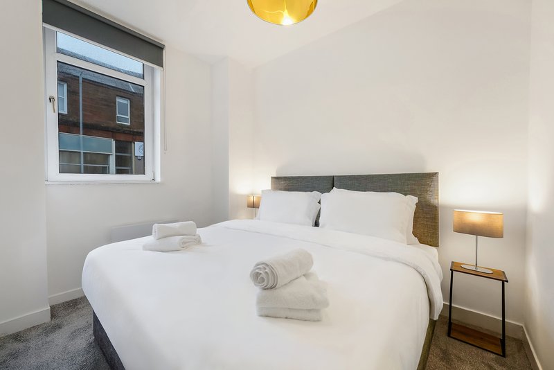 Modern bedroom with double bed, white bedding, wooden headboard, and side lamps