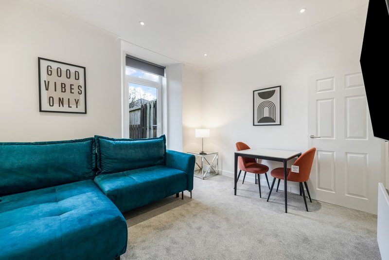 Modern living room with teal corner sofa, wooden dining table, chairs, and framed wall art