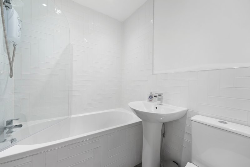 Clean modern bathroom with white subway tiles, bathtub, pedestal sink and shower screen
