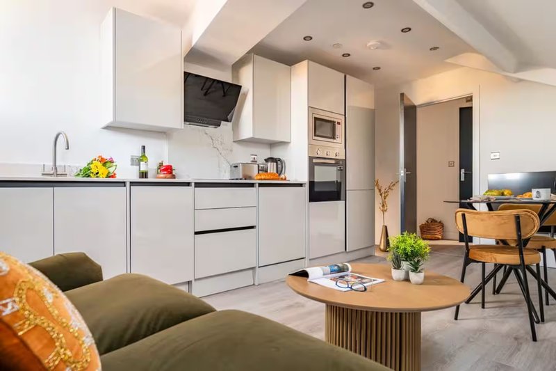 Modern open-plan kitchen and living area with white cabinetry, wooden dining table and green sofa