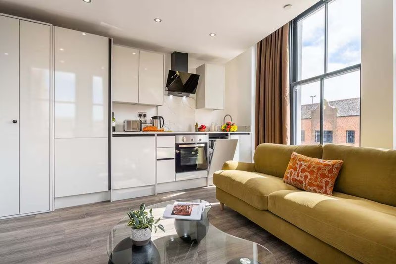 Modern open-plan kitchen and living area with white cabinetry, mustard sofa, and large windows