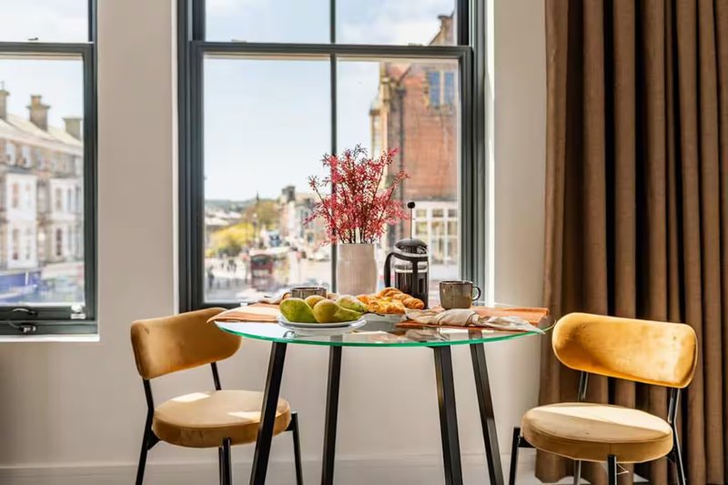 Dining table with two chairs, place settings, flowers, and city view through large windows