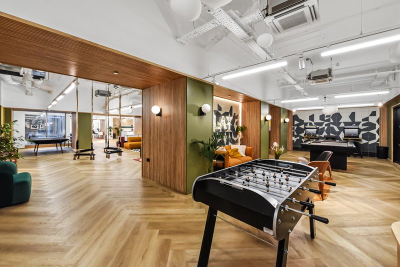 Modern communal space with foosball table, wooden flooring, and glass-partitioned rooms