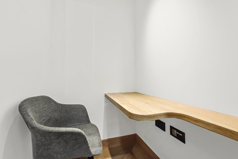 Modern workspace with gray upholstered chair, natural wood floating desk, and white wall