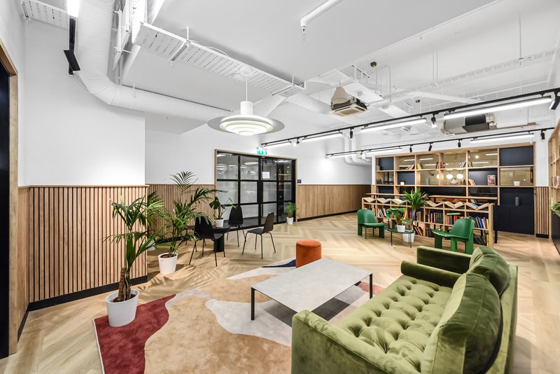 Modern open-plan office space with green sofa, wooden storage shelves and plants