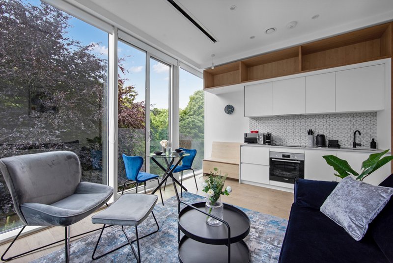 Modern open-plan living space with kitchen, dining area, grey armchair and blue chairs by large windows