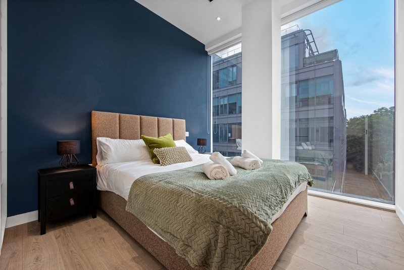 Modern bedroom with double bed, navy accent wall, bedside table, and city views through large windows
